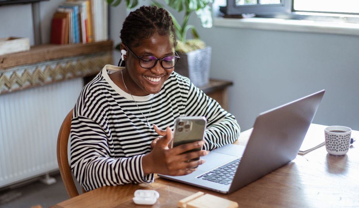 A young woman smiles at her phone while working remote.