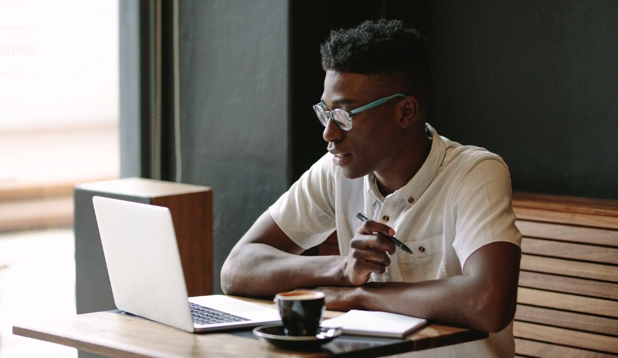 A young man works on his laptop in a coffee shop.